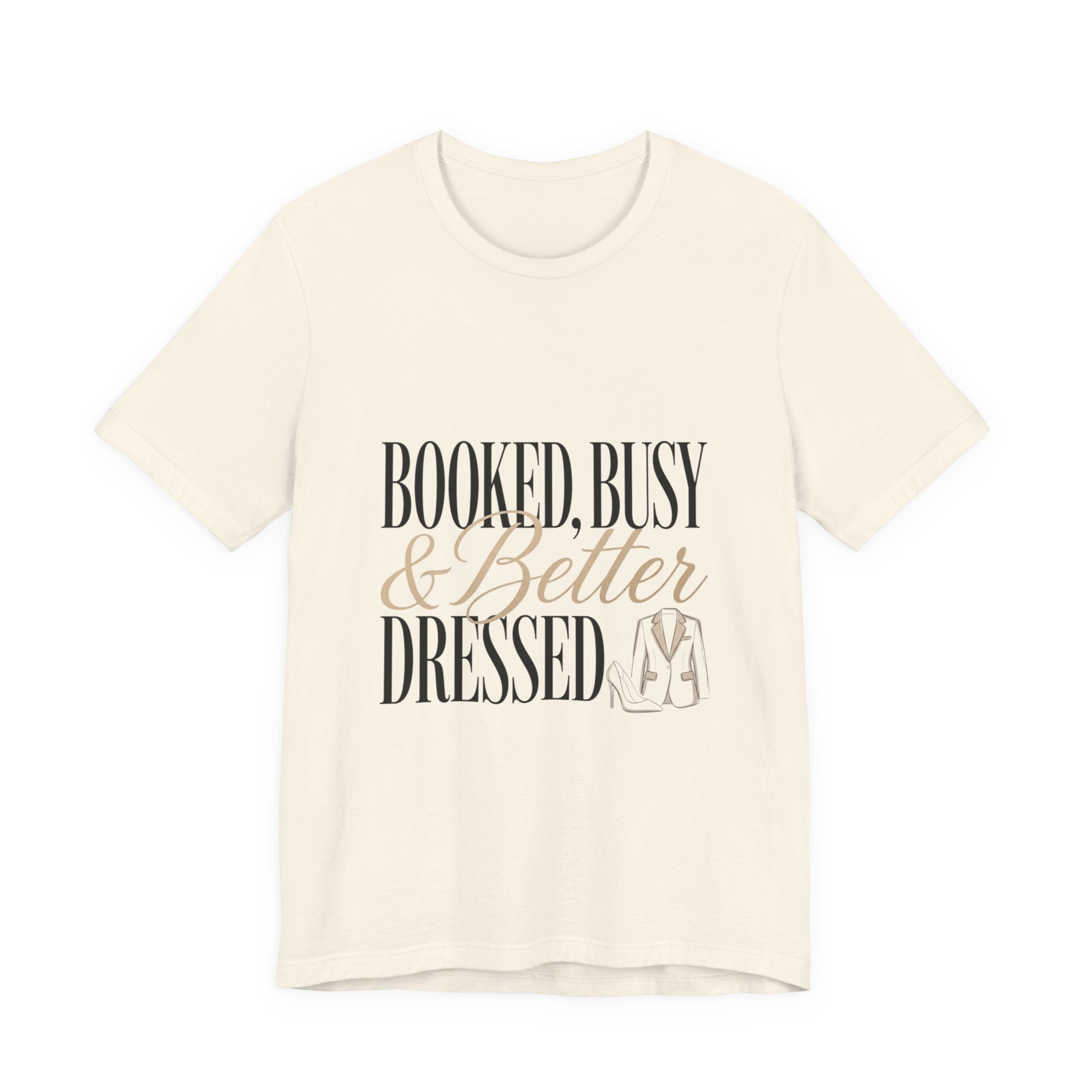 A cream-colored crew neck t-shirt featuring the text Booked, Busy and Better Dressed with a blazer.