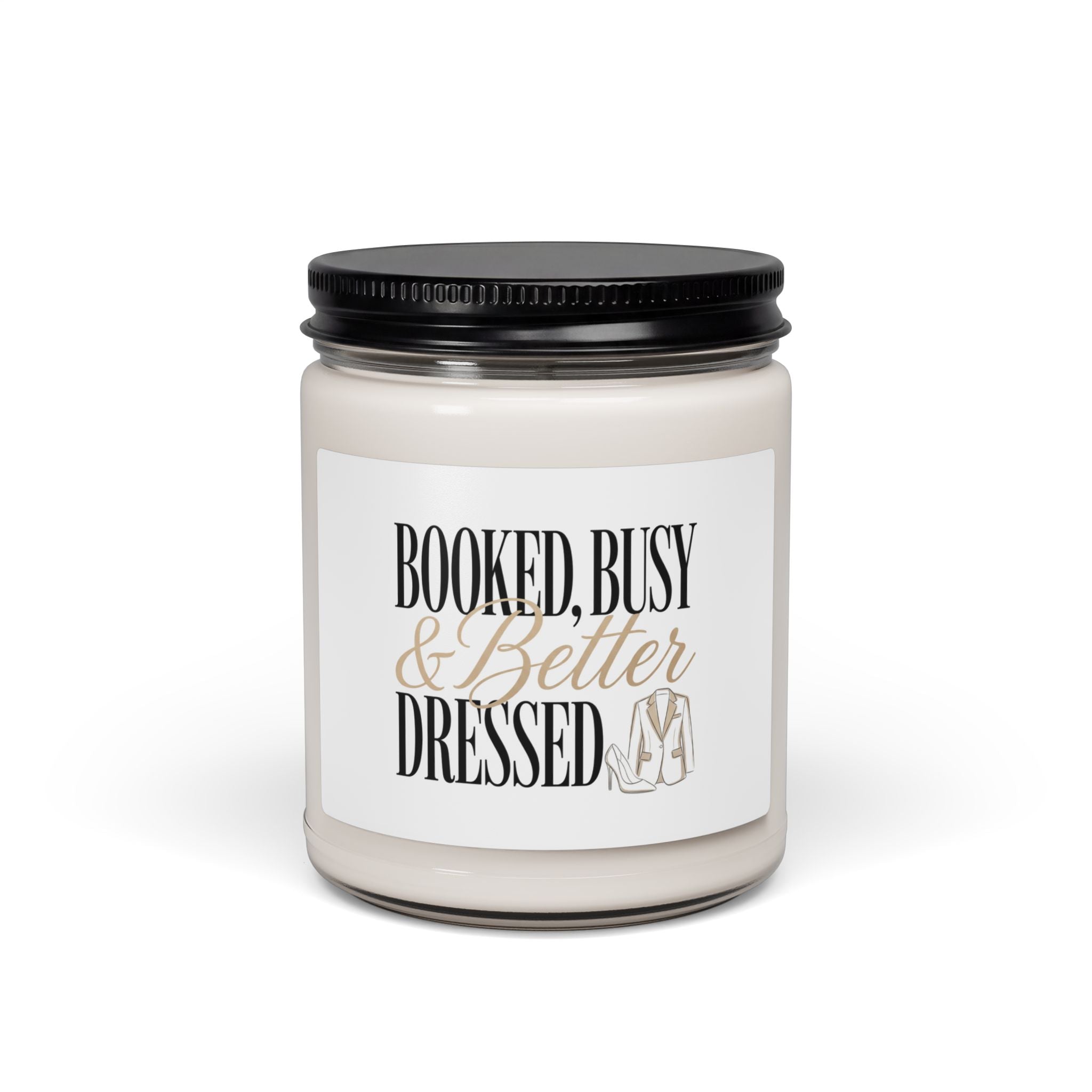 A soy candle in a glass jar with a black lid and a label reading Booked, Busy and Better Dressed.