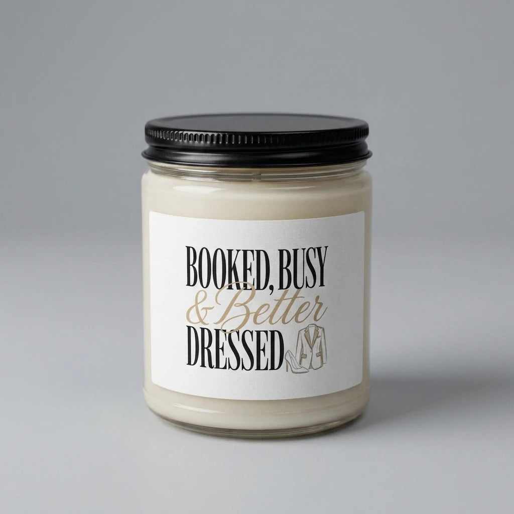 A soy candle in a glass jar with a label that reads Booked, Busy and Better Dressed.