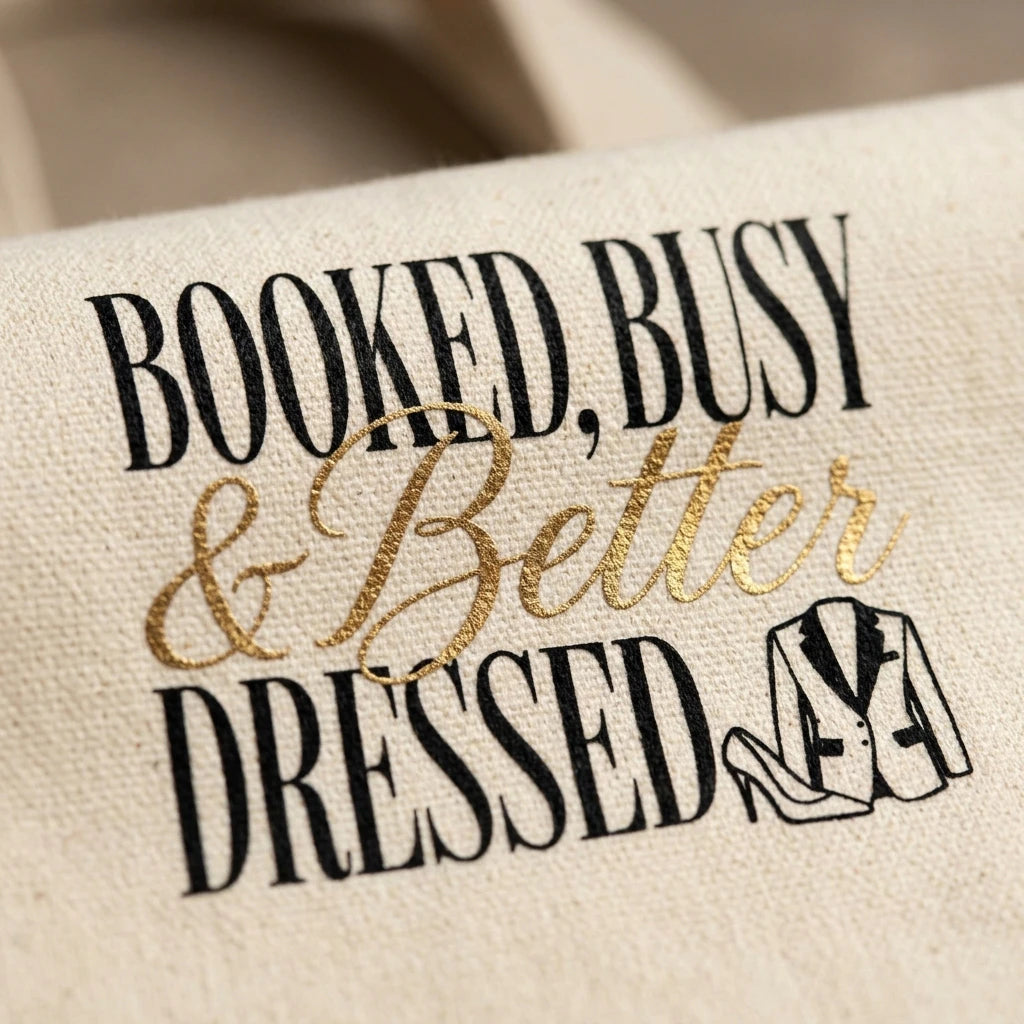 A canvas tote bag featuring the text Booked, Busy and Better Dressed with a tuxedo illustration.