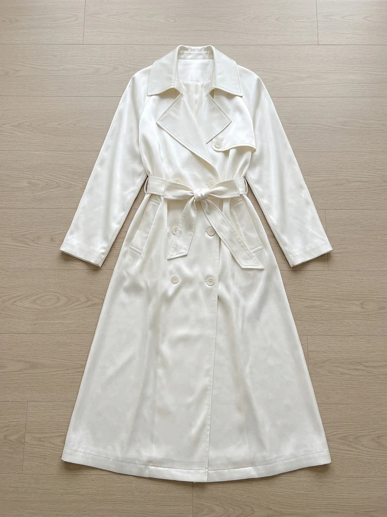 A long, shiny white double-breasted trench coat with a waist sash and lapel collar.