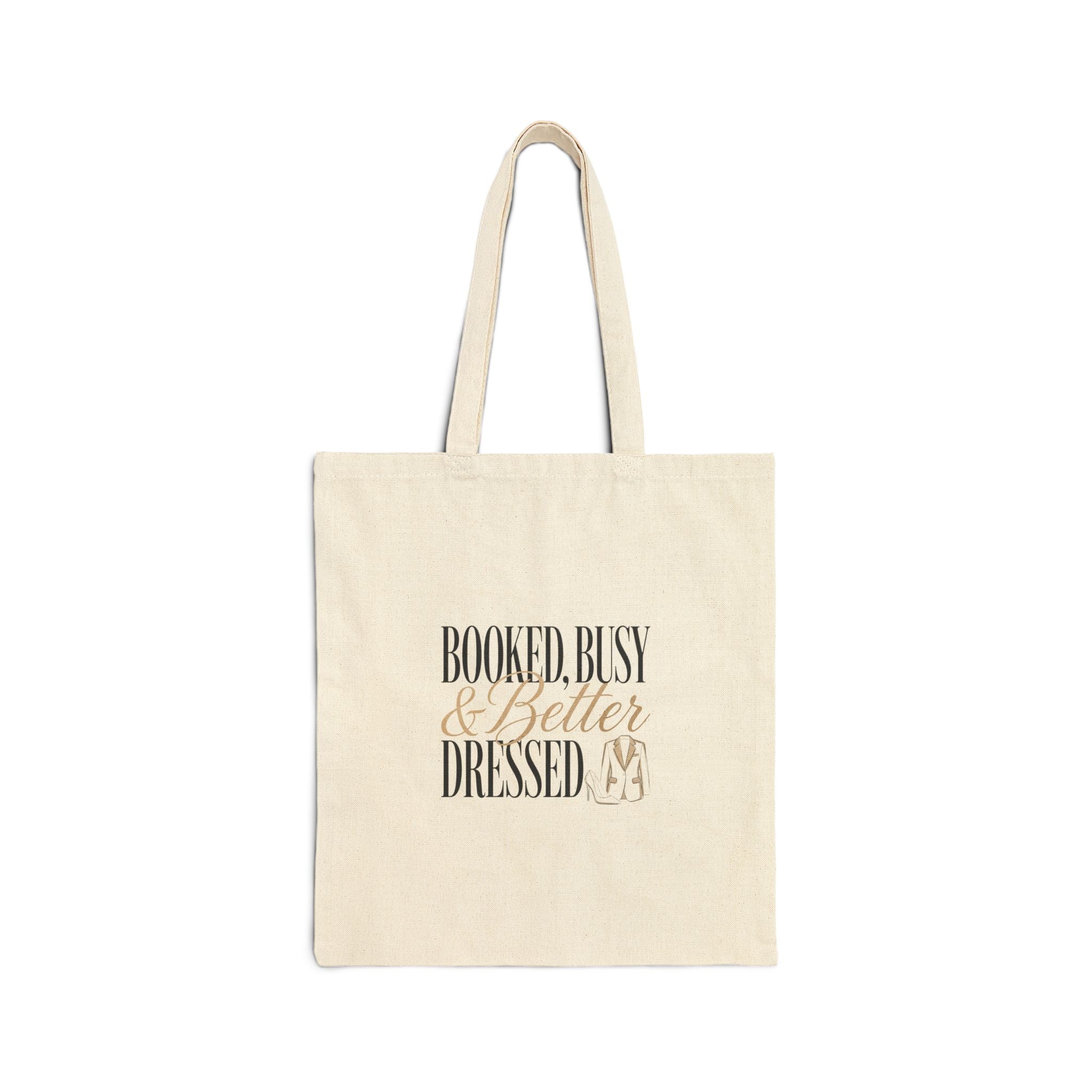 A natural canvas tote bag featuring the text Booked, Busy and Better Dressed with a suit icon.