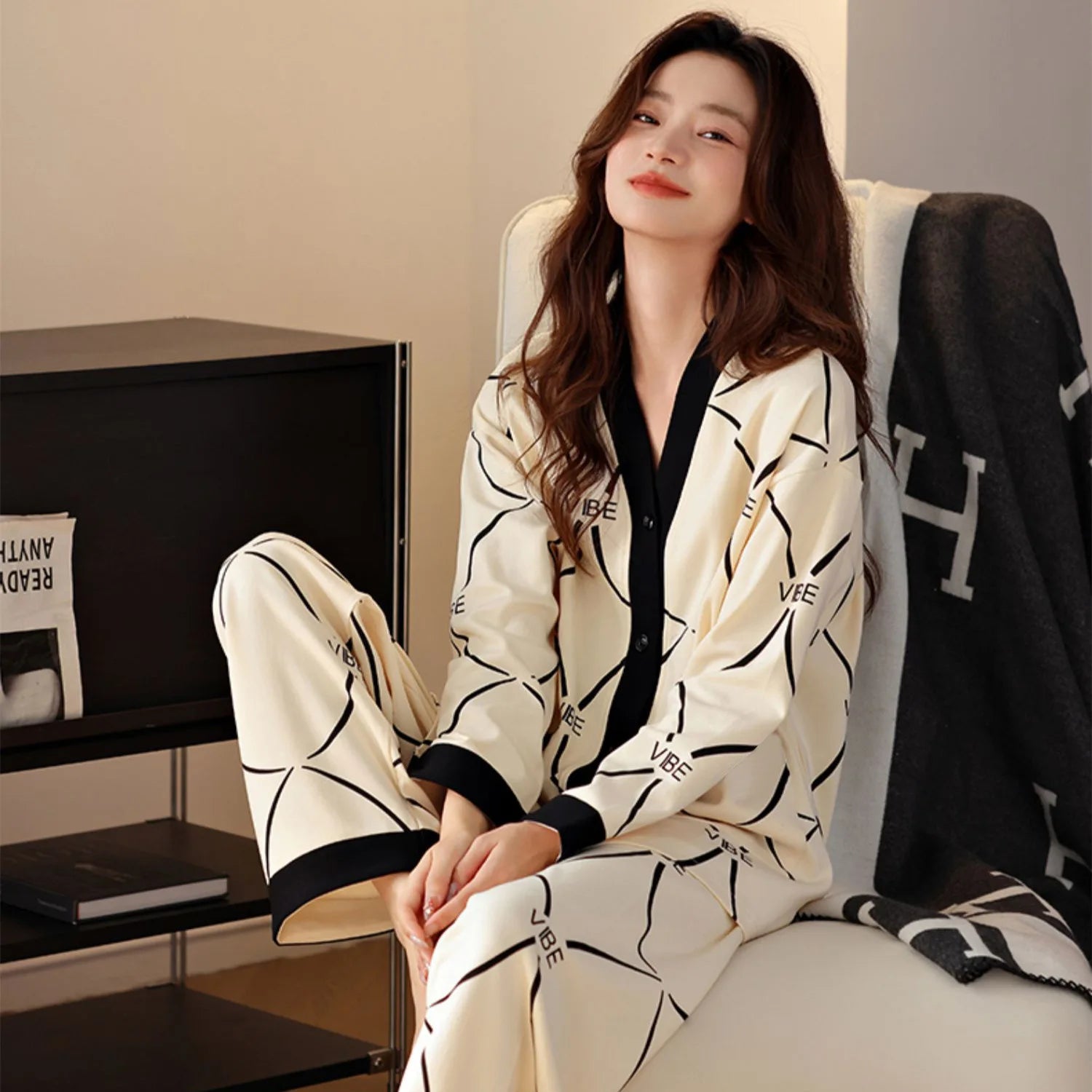 A woman wears a cream-colored long-sleeved pajama set with a black V-neck and geometric print.