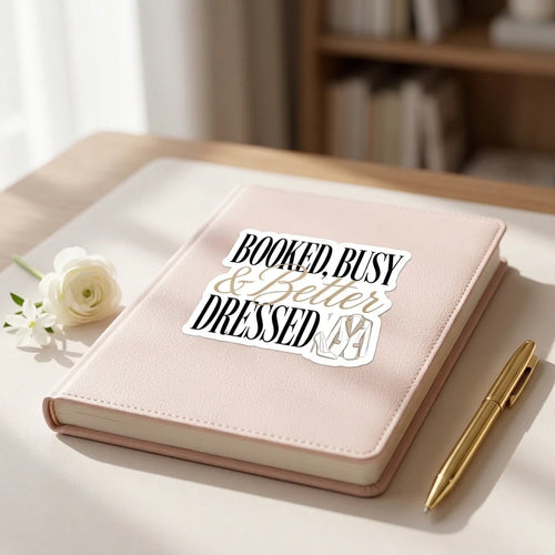 A sticker reading Booked, Busy and Better Dressed with a blazer illustration on a pink journal.