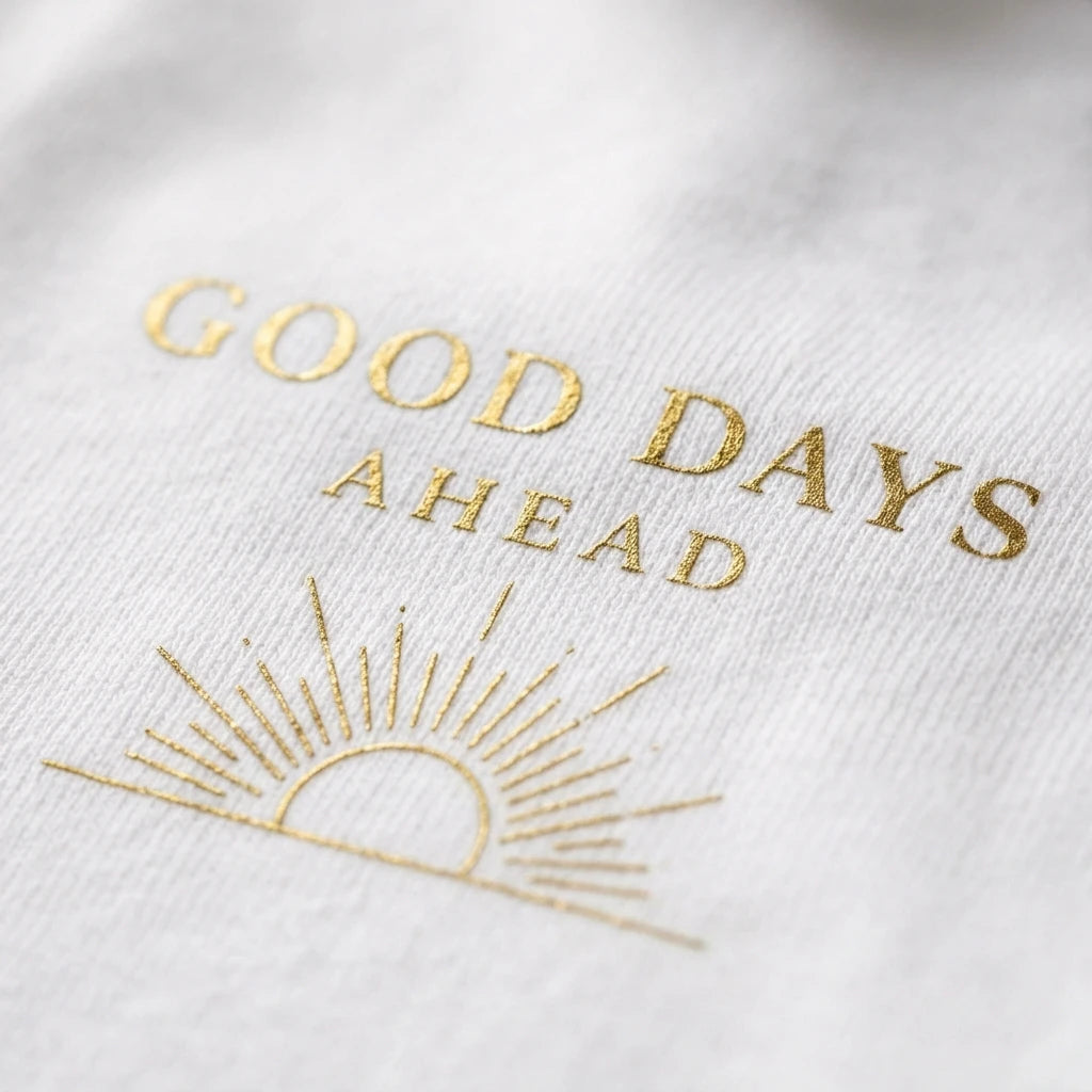 A white t-shirt featuring the gold foil text Good Days Ahead above a gold sun icon.